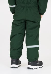 Groene waterdichte overall met elastische manchetten, reflecterende strepen en zwarte schoenen met een gestructureerde zool. Ontworpen voor gebruik buitenshuis.