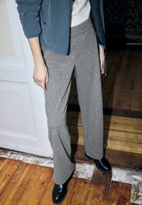 Hellgraue, weit geschnittene Hose aus weichem Stoff mit hohem Taillenbund und lockerem Sitz, kombiniert mit schwarzen Stiefeletten.