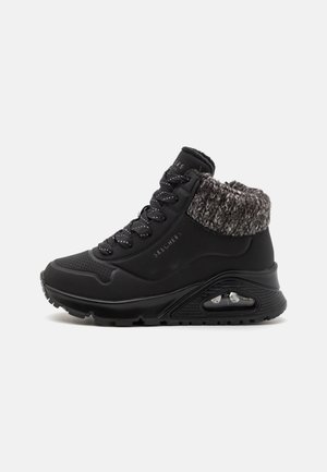 Schwarze High-Top-Sneaker mit einem strukturierten grauen Strickbund, durch perforierte Details, schwarzen Schnürsenkeln und einer sichtbaren Luftpolstersohle.