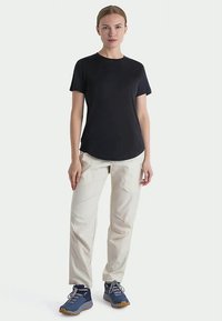 Črna majica s kratkimi rokavi, svetlo bež hlače in modri superge. Gladek material, minimalističen dizajn in udoben kroj.