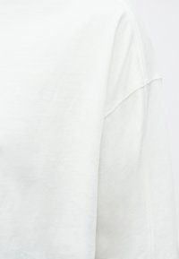 Biała bawełniana bluza z okrągłym dekoltem, opuszczonymi ramionami oraz gładką fakturą z subtelnymi detalami szwów.