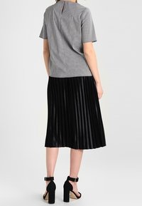 Gonna midi plissettata nera abbinata a una maglietta a maniche corte a quadri. La maglietta presenta un'apertura a forma di chiave sul retro. Scarpe nere con tacco alto.