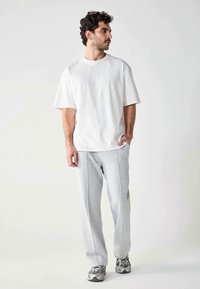 Witte katoenen t-shirt met ronde hals, gecombineerd met lichtgrijze joggingsbroek met verticale naden. Model draagt grijze sportschoenen.