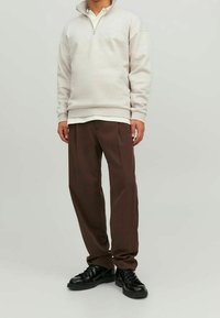 Sudadera de tejido polar gris claro con cuello de media cremallera, combinada con pantalones oscuros de corte tapered y zapatos negros con cordones. Diseño sencillo.