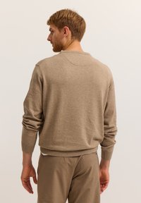 Beige knitted sweater with ribbed cuffs and hem, crew neck design, smooth texture, worn over matching beige trousers, viewed from the back.