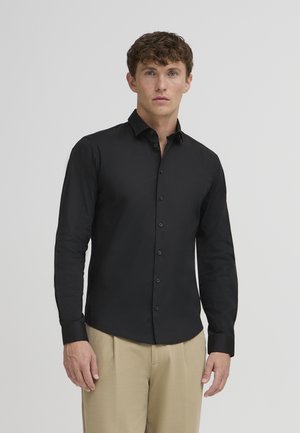 Black long-sleeve shirt with a collar and front buttons, made of smooth fabric. Worn with beige trousers, displaying a fitted design.