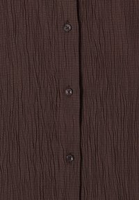 Tissu marron avec une texture froissée et trois boutons foncés alignés verticalement au centre.