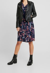 Svart läderbikerjacka lagd över en blommig marinblå klänning. Klänningen har rosa och vita blommor, med ett lätt texturerat tyg. Svarta ankelboots fulländar looken.