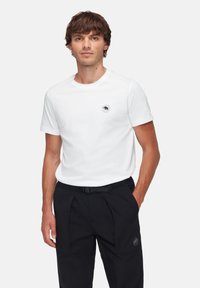 Witte katoenen T-shirt met een ronde halslijn, voorzien van een klein zwart logo op de linkerkant van de borst. Gecombineerd met zwarte broek.