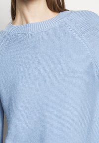 Ljusblå stickad tröja med ribbat runt halsen och raglanärmar, med en texturerad väv och en avslappnad passform.