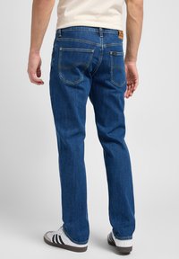 Blå denimjeans med rak passform, med gul sömnad, två bakfickor och en läderlogotyp vid midjan.
