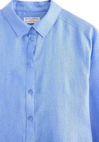Camicia azzurro chiaro con bottoni, dotata di colletto, texture morbida e maniche lunghe. Include sei bottoni lungo la pattina anteriore.