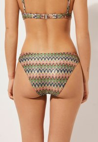Flerfärgad bikini med zigzag-mönster. Mjuk tyg med en glänsande yta. Justerbara remmar och ett spänne bak.