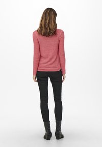 Růžový pletený svetr s dlouhými rukávy, přiléhavý střih a žebrovaný lem. Spárováno s černými skinny džíny a kotníkovými botami.