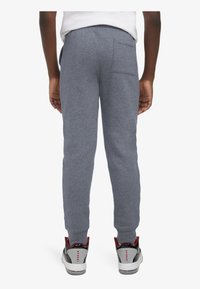 Pantalones de chándal grises con un ajuste ceñido, cintura elástica y un bolsillo trasero. Combinados con zapatillas negras y rojas con detalles en blanco.