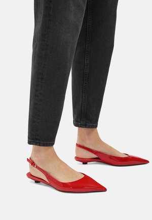Rote Lackleder Slingback-Ballerinas mit spitzen Zehen, ausgestattet mit einem niedrigen Absatz und einem dünnen Knöchelriemen, kombiniert mit schwarzen, taillierten Jeans.