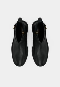 Pár černých kožených kotníkových bot se zipem po straně a zlatou sponou, pohled shora na bílém pozadí.