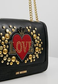 Svart Love Moschino-handväska med guld kedjesträng, dekorerad med ett rött hjärta och guld- och silvernitar som stavar "LOVE."