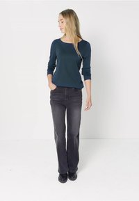 Granatowy, długi rękaw bluzka połączona z czarnymi dżinsami. Strój charakteryzuje się luźnym krojem i jednolitym kolorem, a model stoi w neutralnym otoczeniu.