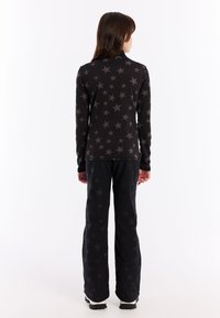 Haut à manches longues noir avec un motif d'étoiles grises, associé à un pantalon noir présentant un design similaire. Tissu texturé, coupe décontractée et matériel minimal.