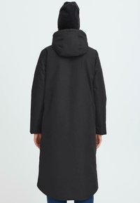 Svart vadderad jacka med huva, långa ärmar och rak passform. Har en slät yta och en rundad fåll bak.