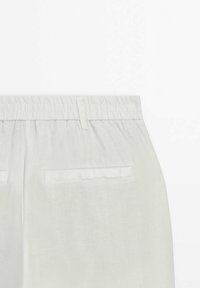 Pantalon en lin blanc avec une taille élastique froncée, doté de deux poches arrière et d'un tissu doux et texturé. Design simple et fonctionnel.