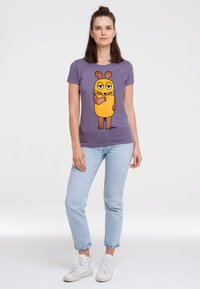 Purple t-shirt featuring a cartoon character with an orange body and brown accents, paired with light blue jeans and white sneakers.