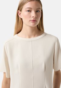 Kurzarmpullover aus cremfarbener, glatter Stoffqualität mit rundem Halsausschnitt, verziert mit feinen Nähten und einer lässigen Passform.