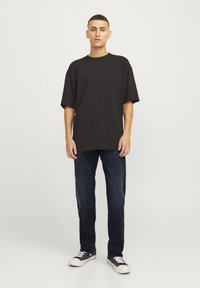 Camiseta negra oversize de algodón, combinada con vaqueros azul oscuro. El conjunto se completa con zapatillas de deporte en blanco y negro.