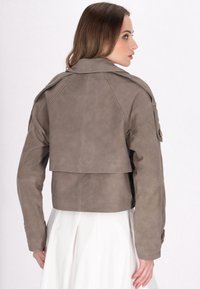 Giacca in pelle taupe tagliata, dal design aderente, con ampio colletto e spalline; texture liscia con una finitura pulita.