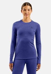 Long-sleeve athletic shirt in deep purple, made of a smooth, fitted fabric. Features a round neck and subtle logo on the chest.