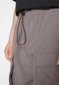 Šedé cargo šortky s elastickým pasem, nastavovací šňůrkou a bočními kapsami. Hladký povrch a jednoduchý design.