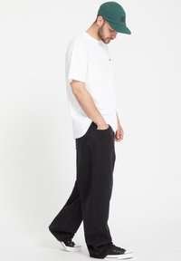 Hvit kortermet t-skjorte, løse svarte denim-bukser, grønn caps og svarte joggesko. Antrekket har en avslappet passform med et enkelt design.