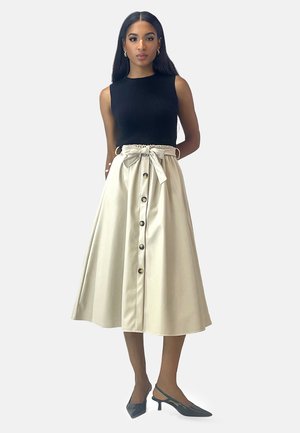 Schwarzes, geripptes, ärmelloses Oberteil, kombiniert mit einem beigen A-Linien-Rock, der eine Knopfleiste und eine gebundene Taille hat. Dazu passende blaue Absatzschuhe.
