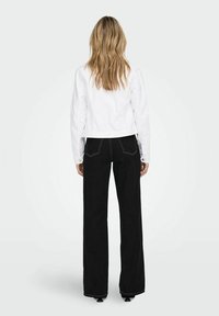 White cropped jacket with long sleeves, paired with black wide-leg trousers featuring contrasting white stitching and flared hems.