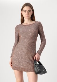 Vestido de malha castanho cintilante com mangas compridas e decote canelado, apresentado com brilhos metálicos. Acompanha uma bolsa preta.