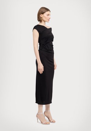 Robe noire ajustée avec un design enveloppant au niveau de la poitrine et de courtes manches. Tissu lisse, jupe arrivant au genou, assortie à des sandales à talons transparents.