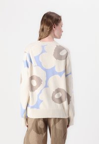 Pinums ad krema krāsu ar zilu un brūnu ziedu rakstu, ribotām piedurknēm un apaļu kakla izgriezumu. Palielināts izmērs, gluda tekstūra, neformāls dizains.