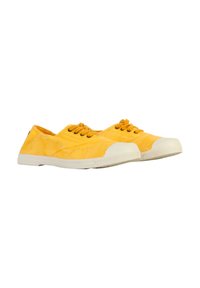 Zapatillas de lona amarillas con suelas de goma blanca, que presentan una punta redonda, acentos cosidos y cinco ojalillos para los cordones.