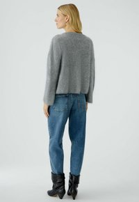 Grijs, fluffy gebreid sweater met een ronde halslijn, gecombineerd met losse blauwe spijkerbroeken en zwarte enkellaarsjes, gezien vanaf de achterkant.