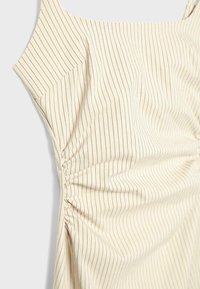 Haut sans manches couleur crème avec de fines rayures verticales marron et un détail froncé sur le côté.