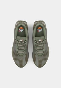 Green sneakers with a textured, glossy finish, featuring round laces, mesh panels, and visible branding on the insoles.