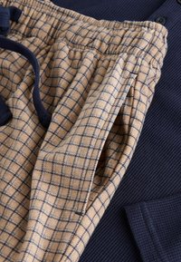 Beige and navy checkered loungewear pants with an elastic waist and drawstring. Ribbed navy fabric visible behind the pants.