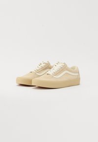 Beige mokasiner avsuede med lyse kremfarger og snøringer, med en flat, teksturert gummisåle og lavt design.