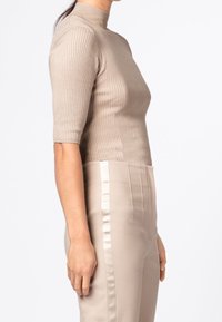 Dopasowany, prążkowany, beżowy top z wysokim stójką i krótkimi rękawami, w zestawieniu z wysokim stanem, gładkimi, kremowymi spodniami.