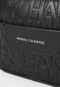 Schwarze, strukturierte Lederhandtasche mit geprägtem "ARMANI EXCHANGE"-Logo, ausgestattet mit einem glatten Einsatz mit silberner Schrift und geometrischen Mustern.