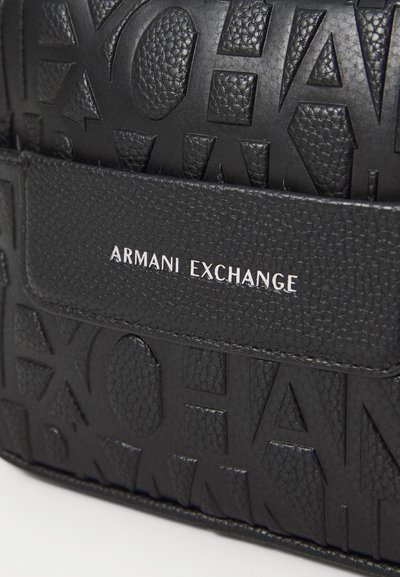 Черен текстуриран кожен сак с релефно лого "ARMANI EXCHANGE", притежаващ гладка лента със сребърно писмо и геометрични мотиви.