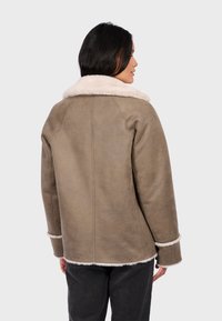 Brown suede jacket with a white fur collar and cuffs. Features a relaxed fit and visible stitching along seams. No fastenings shown.