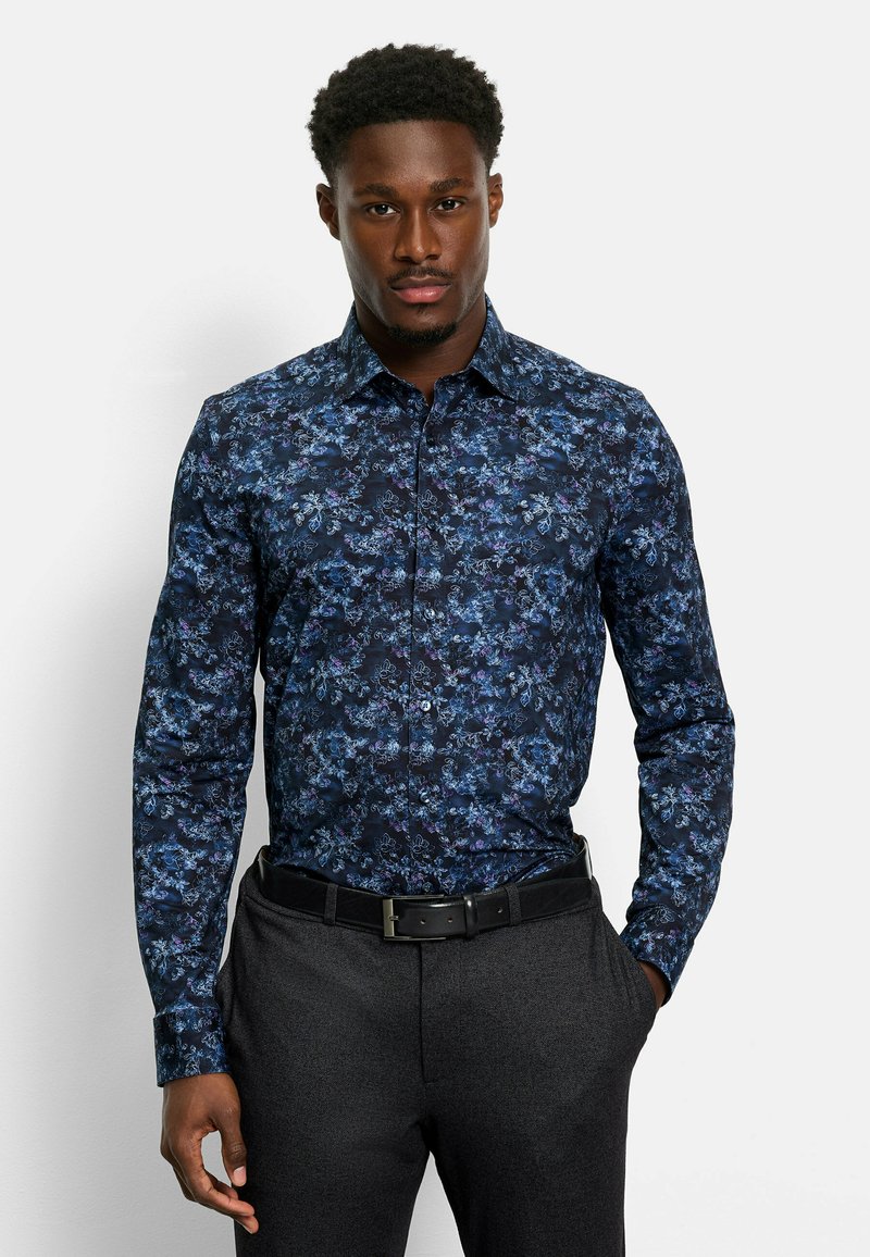 Dunkelblauses Hemd mit floralem Muster, langen Ärmeln, Button-Down-Kragen und kontrastierenden Farben. Getragen mit dunklen Anzughosen und einem Gürtel.