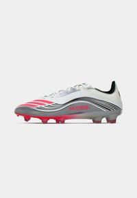 Hvide og grå fodboldstøvler med pink accenter, der har en meshuoverdel, struktureret design og formede riller for godt greb. "MESSi" logo er til stede.